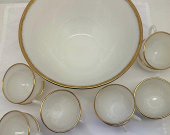 May include: A set of white milk glass punch bowl and cups with gold trim. The bowl is large and round, and the cups are smaller and have handles.