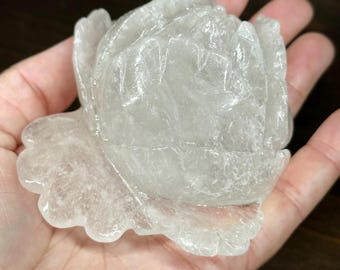 May include: A clear quartz crystal carved into the shape of a rose. The rose is detailed with petals and leaves.
