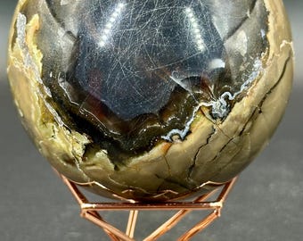 May include: A polished, brown and black agate sphere on a copper-colored metal stand. The sphere has a unique, swirling pattern and a dark center.