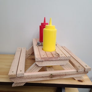 Pode incluir: Uma mesa de piquenique de madeira em miniatura com duas garrafas de condimento, uma vermelha e uma amarela, no centro.