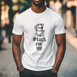 May include: White t-shirt with a black graphic of stacked coffee cups and the text "Stack em up" in a gothic font. The text "Breakfast/Lunch/Dinner" is written in cursive below the graphic.