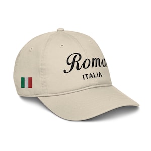 Könnte beinhalten: Eine beige Baseballkappe mit schwarzem Sticktext "Roma ITALIA" und einer kleinen italienischen Flagge an der Seite.