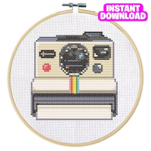 May include: A cross-stitch pattern of a vintage Polaroid camera with a rainbow stripe across the lens. The camera is white with black and gray details.