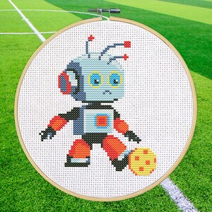 Puede incluir: Un patrón de punto de cruz de un robot jugando al fútbol. El robot es azul, gris y naranja, y está pateando un balón de fútbol amarillo y naranja. El robot tiene una expresión amigable en su rostro.