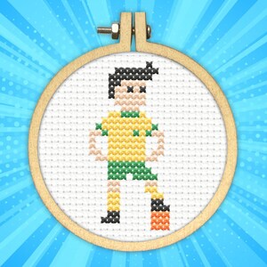May include: Cross-stitch embroidery hoop with a colorful pixelated design of a soccer player in a yellow and green jersey, kicking a black and orange soccer ball.