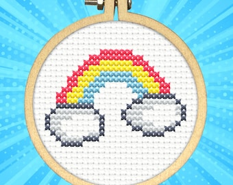 May include: A cross-stitch embroidery hoop featuring a colorful rainbow design. The rainbow arches across the center, with red, yellow, and blue hues. Fluffy white clouds are at each end. The hoop is made of light-colored wood.