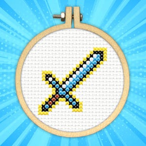 以下が含まれることがあります： 青いピクセルと黄色の剣のデザインが施されたクロスステッチ刺繍フープ。剣は白い背景になっています。