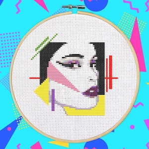 Peut inclure: Un cerceau de broderie au point de croix avec un motif géométrique coloré d'un visage de femme. Le motif comprend du rose, du jaune, du violet, du vert et du noir.