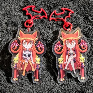 May include: Two red and pink anime character keychains with a red bat wing design. The characters are sitting on a throne with a red and gold design.