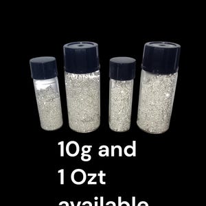 May include: Four clear glass bottles with black lids filled with silver glitter. The bottles are of different sizes. Text on the image reads "10g and 1 Oz available."