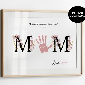 May include: Framed print with the word "MOM" in black letters, with a pink handprint replacing the "O". The letters are decorated with pink floral accents. The text "She is more precious than rubies" and "Love Kinsley" are also included.