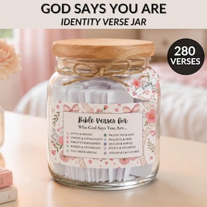 Pode incluir: Um frasco de vidro transparente com tampa de madeira clara, cheio de tiras de papel branco. O rótulo apresenta padrões florais, laços e o texto Bible Verses for Who God Says You Are. Uma etiqueta em forma de coração diz Emily.