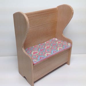 May include: A wooden bench with a high back and a patterned cushion. The bench is made of light wood and has a simple design.