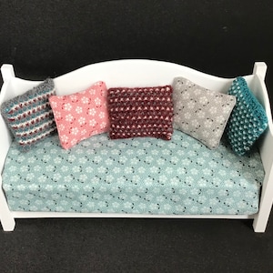 May include: A white daybed with a blue and white patterned mattress and five colorful crocheted pillows. The pillows are in shades of pink, gray, teal, and burgundy.
