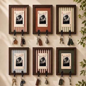 Puede incluir: Seis soportes de pared para llaves de madera oscura, cada uno con un gráfico de carta de juego con una foto de pareja y el texto How lucky are we. Cada marco tiene dos ganchos de metal negro que sostienen varias llaves y colgantes.