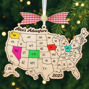 Könnte beinhalten: Holzschmuck in Form der Vereinigten Staaten, wobei jeder Staat umrissen ist. Die Staaten WA, NV, CO, IA und OH sind farbig. Der Schmuck hat eine rot-weiß karierte Schleife und den Text "Alex's Adventure" und "2025".