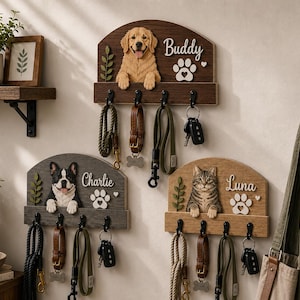 K&ouml;nnte beinhalten: Drei wandmontierte Holzorganizer mit skulptierten Tierfiguren: ein Golden Retriever namens Buddy, eine Franz&ouml;sische Bulldogge namens Charlie und eine getigerte Katze namens Luna. Jede Einheit hat vier schwarze Metallhaken f&uuml;r Leinen und Schl&uuml;ssel.