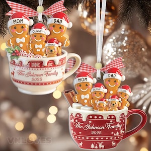 Könnte beinhalten: Zwei Weihnachtsschmuck-Anhänger in Tassenform, gefüllt mit Lebkuchenfiguren und Haustieren. Jede Tasse trägt die Aufschrift The Johnson Family 2025, rot-weiße Muster und ein rotes Vichy-Karo-Band zum Aufhängen an der Oberseite.