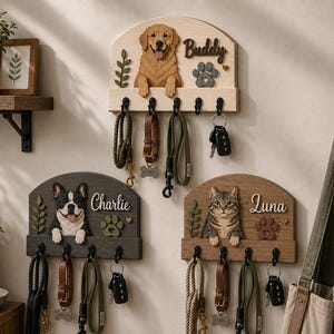 K&ouml;nnte beinhalten: Drei wandmontierte Leinen- und Schl&uuml;sselhalter aus Holz mit geschnitzten Tierfiguren. Das obere Brett zeigt einen Golden Retriever namens Buddy, w&auml;hrend die unteren Bretter einen Boston Terrier namens Charlie und eine getigerte Katze namens Luna zeigen.