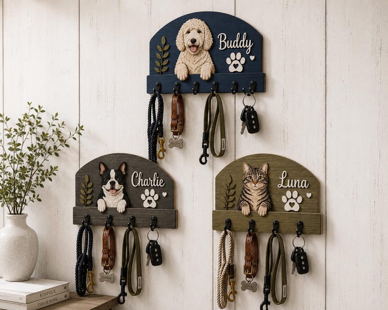 K&ouml;nnte beinhalten: Drei wandmontierte Leinen- und Schl&uuml;sselhalter aus Holz mit geschnitzten Figuren eines Golden Doodles, einer Franz&ouml;sischen Bulldogge und einer getigerten Katze. Jedes Brett zeigt einen Namen, eine Pfote und einen Zweig mit f&uuml;nf schwarzen Haken.