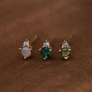 Peut inclure: Trois boucles d'oreilles en or avec une seule pierre précieuse et deux petites pierres claires. Les pierres précieuses sont blanches, vertes et vert clair.