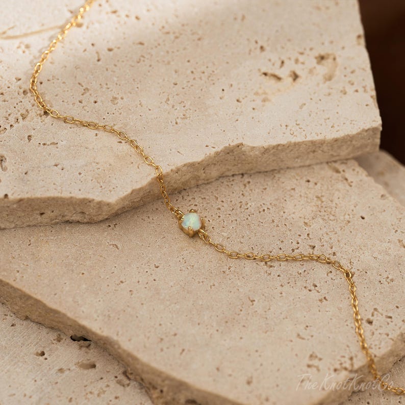 May include: A delicate gold chain bracelet with a single white opal gemstone.