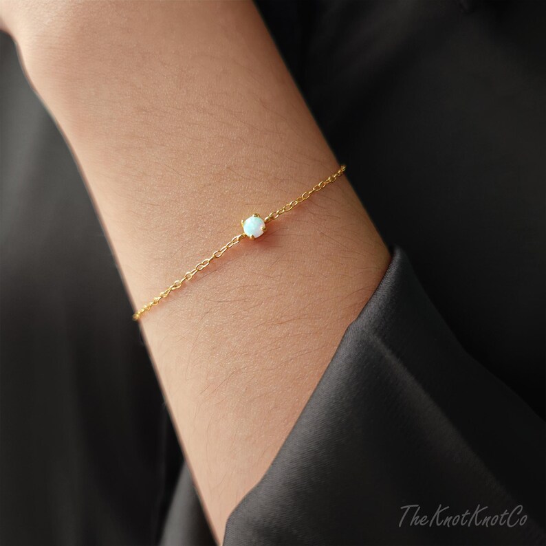 May include: A delicate gold chain bracelet with a single white opal gemstone. The bracelet is simple and elegant, perfect for everyday wear.