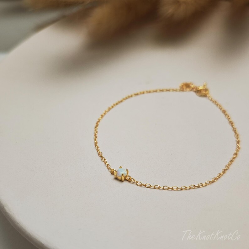 May include: A delicate gold chain bracelet with a single white opal gemstone. The bracelet is simple and elegant, perfect for everyday wear.
