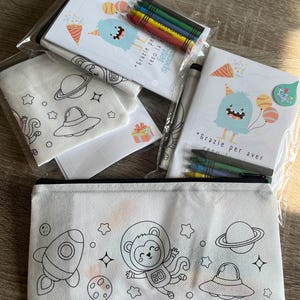 Può includere: Un astuccio bianco e un set da colorare con illustrazioni a tema spaziale. Il set include un astuccio con un design di razzo spaziale e scimmia astronauta, pagine da colorare, pastelli e il testo "Grazie per aver reso la festa speciale."