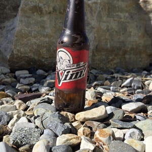 May include: A brown glass bottle with a red label featuring the text "You've got Vim!" and a cartoon image. The bottle is on a bed of rocks, with a large rock and blue sky in the background.