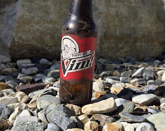 May include: A brown glass bottle with a red label featuring the text "You've got Vim!" and a cartoon image. The bottle is on a bed of rocks, with a large rock and blue sky in the background.