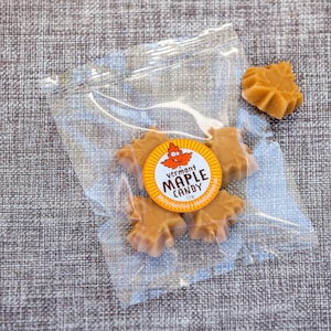 May include: A clear plastic bag filled with maple leaf-shaped candies. The candies are a light brown color and have a sticker on the bag that says "Vermont Maple Candy".