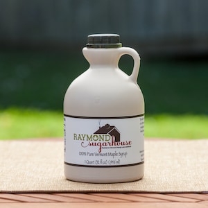 May include: A white plastic jug of 100% pure Vermont maple syrup from Raymond Sugarhouse. The jug is labeled with the company's name and logo, and it contains 32 fluid ounces (946 ml).