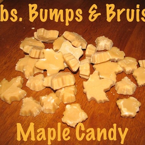 May include: A close-up of 4 lbs of maple candy shaped like maple leaves. The candy is a light brown color and is scattered on a wooden surface. The text "4 lbs. Bumps & Bruises Maple Candy" is written in yellow letters on the top of the image.