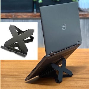 May include: A black laptop computer is propped up on a black, X-shaped stand. The laptop is open and angled, with the Dell logo visible on the back. The stand appears to be made of metal or a similar material.