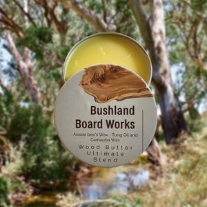Könnte beinhalten: Eine weiße Dose mit braunem Holzmaserungsmuster und dem Text "Bushland Board Works" in Schwarz. Der Text darunter lautet "Aussie bee's Wax - Tung Oil and Carnauba Wax Wood Butter Ultimate Blend".