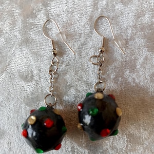 Peut inclure: Paire de boucles d'oreilles noires faites à la main. Chaque boucle d'oreille présente une perle sphérique sombre ornée d'accents rouges, verts et dorés. Les perles sont suspendues à des chaînes et des crochets d'oreilles argentés, créant un accessoire unique.