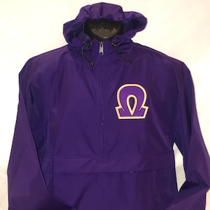 May include: Purple hooded jacket with a gold and purple Omega symbol on the front. The jacket has a zipper closure and a Champion logo on the sleeve.