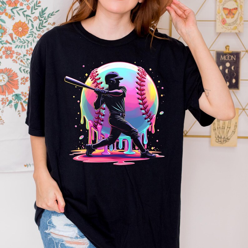 May include: Black t-shirt featuring a baseball player silhouette swinging a bat. A colorful baseball graphic with dripping paint effect is behind the player. The word "MASH" is at the bottom of the graphic.
