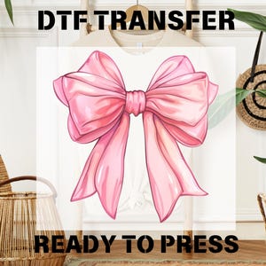 May include: A pink bow with a white background. The text "DTF TRANSFER READY TO PRESS" is printed below the bow.