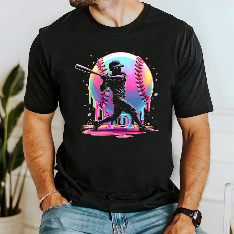 May include: Black t-shirt featuring a vibrant graphic of a baseball player swinging a bat. The design includes a colorful baseball with dripping paint effect. The player is in silhouette, adding a dynamic feel to the sports-themed apparel.