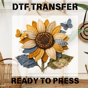 May include: A sunflower DTF transfer ready to press. The sunflower has a brown center, yellow, tan, and blue petals, and green leaves. Two fabric butterflies are attached to the design. The words "DTF TRANSFER" and "READY TO PRESS" are printed in black.