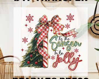 May include: White t-shirt with a Christmas-themed design. The design includes a Christmas tree, a red and white checkered bow, and the phrase "'Tis the Season to be Jolly". Red snowflakes and stars complete the festive look. The text "DTF TRANSFER" and "READY TO PRESS" are also visible.