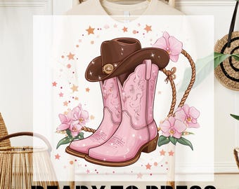 May include: A white t-shirt with a pink and brown cowboy boot design. The boots are decorated with stars and flowers. The text "READY TO PRESS" is printed on the bottom of the shirt.