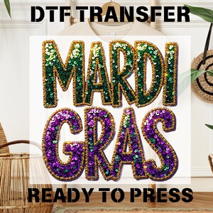 May include: A Mardi Gras themed iron-on transfer with green, purple, and gold sequins. The transfer reads "Mardi Gras" and is ready to press.