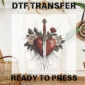 May include: A white t-shirt with a design of a red heart pierced by a sword, surrounded by roses and leaves. The text "DTF TRANSFER" is at the top of the image and "READY TO PRESS" is at the bottom.