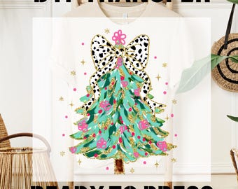 May include: White t-shirt featuring a Christmas tree design. The tree is teal with gold glitter accents and pink floral ornaments. A black and white spotted bow tops the tree. The text "DTF TRANSFER" and "READY TO PRESS" are displayed.