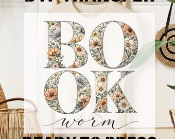 May include: A white t-shirt with the words "BOOK WORM" in large floral letters. The letters are filled with pastel-colored flowers. The words "DTF TRANSFER" and "READY TO PRESS" are printed above and below the main text.