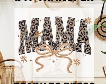 May include: White t-shirt with the word "MAMA" in a leopard print design, accented with a bow and floral elements. The text "DTF TRANSFER" and "READY TO PRESS" are displayed above and below the main design.