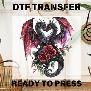 May include: DTF TRANSFER graphic featuring two intertwined black dragons forming a heart shape, with red roses and the text "READY TO PRESS". The dragons have red and purple wings, and the design is on a white background.